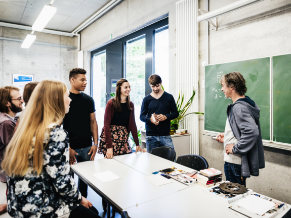 Foto in einer Lehranstalt mit mehreren Personen und einer Tafel