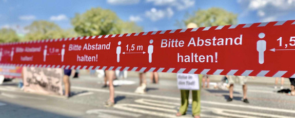 Rotes Absperrband bei Demonstration mit Hinweis "Bitte Abstand halten"