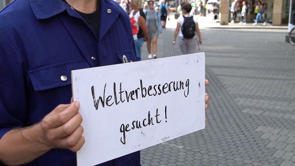 Ein Mann mit einem Schild: Weltverbesserung gesucht