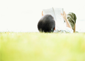 Junge liegt im Gras und liest Buch.